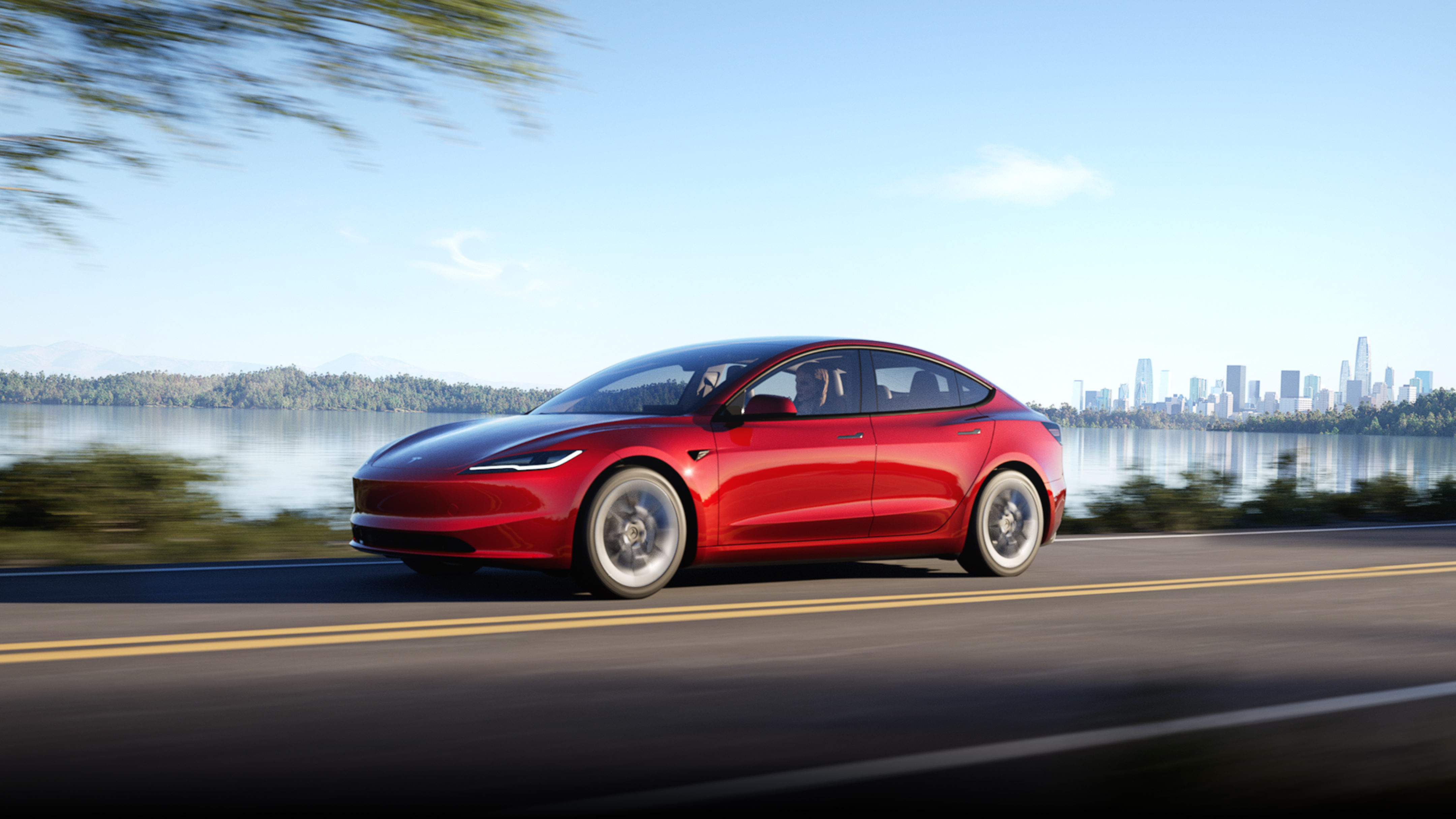 以城市景觀為背景的烈焰紅 Model 3 行駛在道路上。