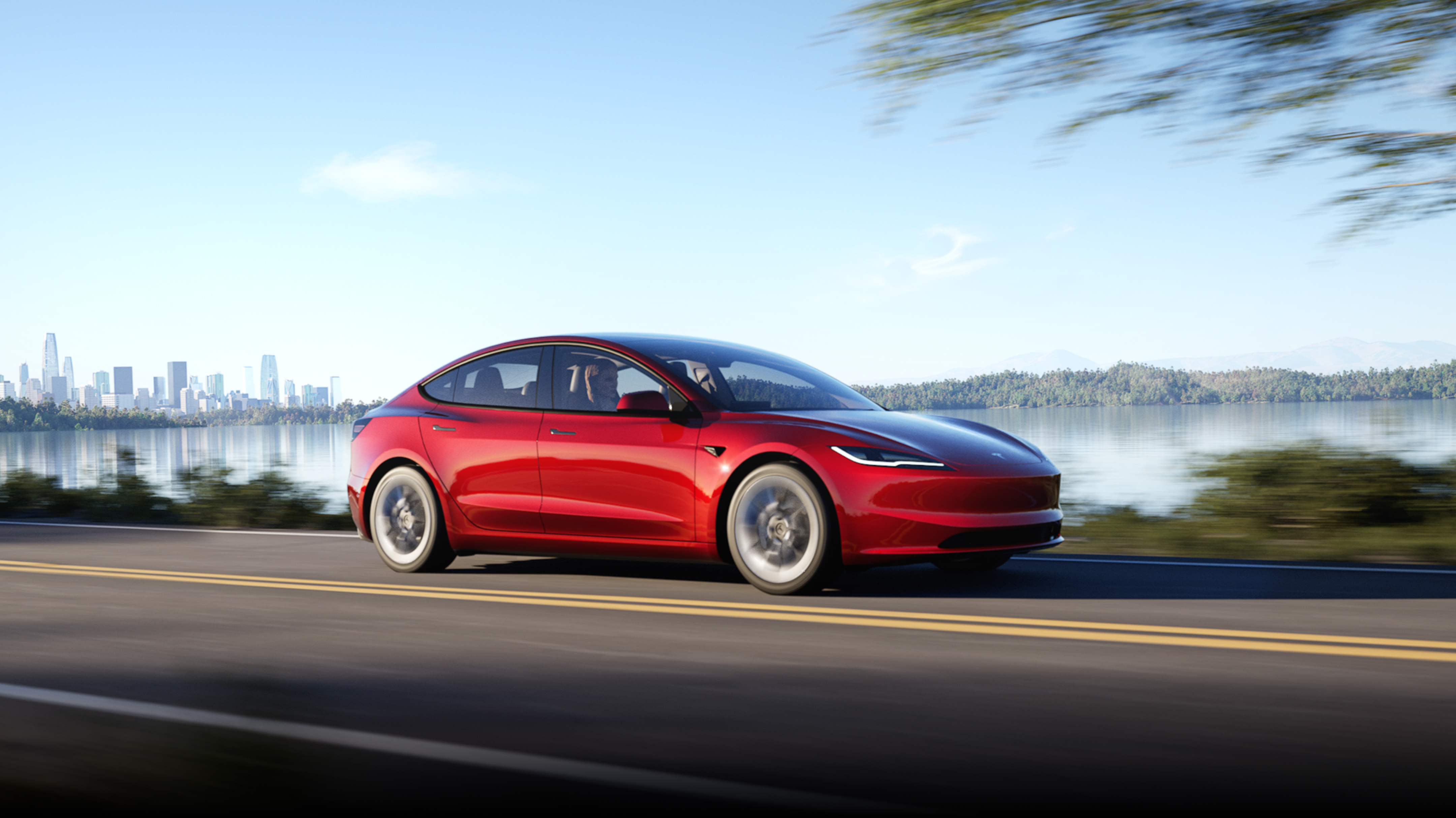 Model 3 สี Ultra Red กำลังวิ่งไปตามถนนที่มีเมืองเป็นฉากหลัง